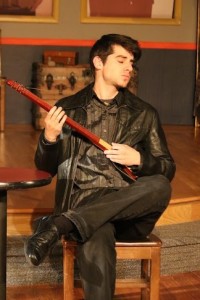 Matt Payne as Marcel, playing his Strumstick for Deedee in 13 Dead Husbands at Cohesion Theatre Company