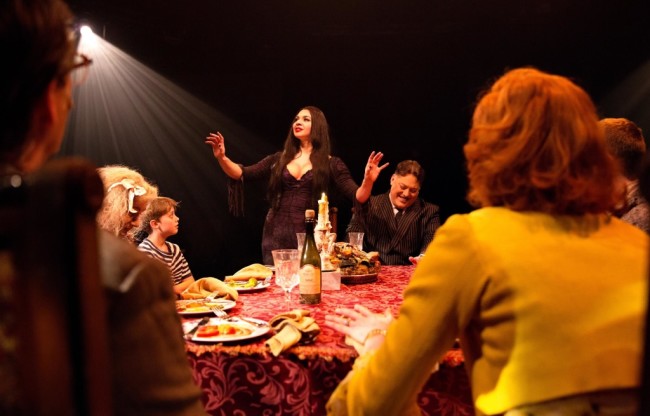 Morticia (Center Left- Priscilla Cuellar) prepares the family game, Full Disclosure, as husband Gomez Addams (Center Right- Lawrence B. Munsey) frets over his own Full Disclosure.