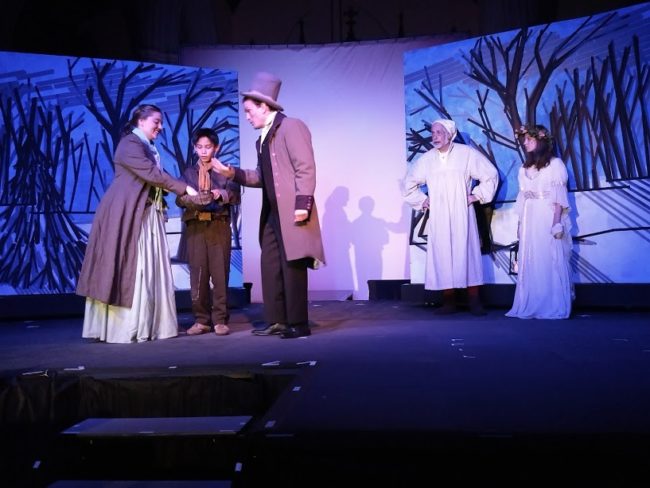 (L to R) Karissa Strawley Bryant as Bell, Alexander Walston-Valdas as caroling orphan boy, Ewan MacLean as Young Man Ebenezer, Richard Peck as Ebenezer Scrooge, and Petra McGregor as the Ghost of Christmas Past