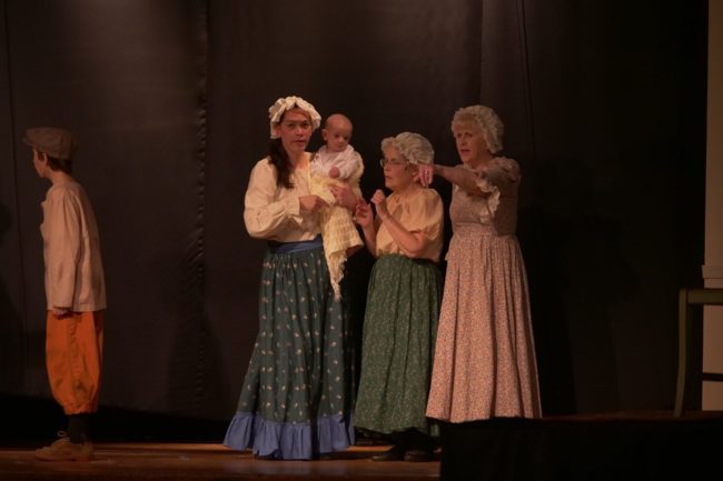 Kristy Wiggins (left) holding the youngest member of a St. Gabriel Miracle Players' production to ever appear on stage, Joshua Wiggins, at not-quite-six months old, as street ensemble members in Oliver! 