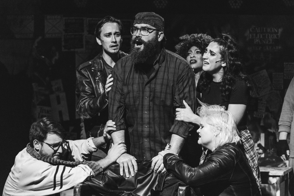 Ryan Wagner (center) as Tom Collins and the company of Rent. 📸Matthew Peterson