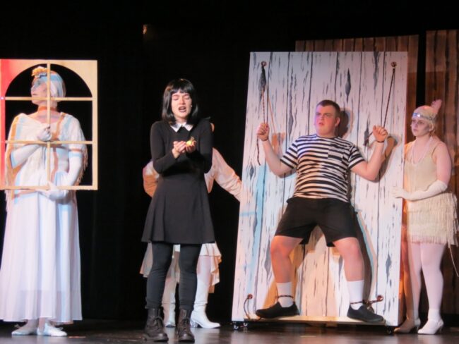 Mo Tacka (center left) as Wednesday and Ethan Buttman (on the rack) as Pugsley 📷 Cathy Herlinger
