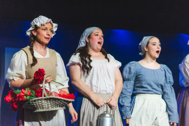 Lisa Rigsby Geiger (left) as Rose Seller, with Amy M. Tucker (center) as Milkmaid and Anna Odell (right) as Milkmaid in Oliver! at Tidewater Players 📷 Matthew Peterson