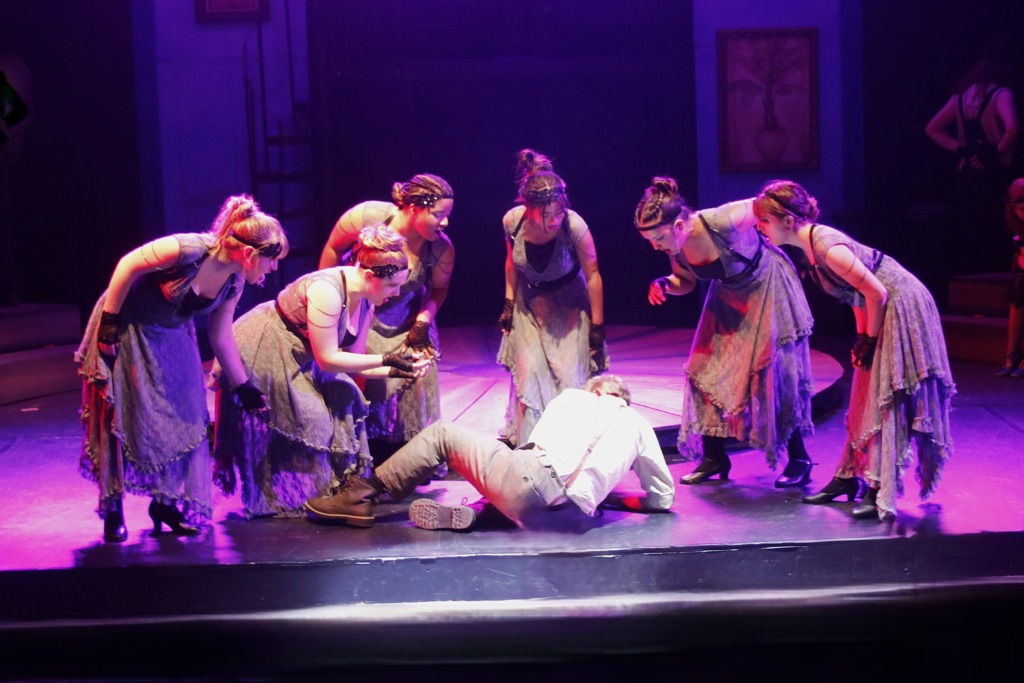 The Fates (L to R) Kaitlyn Bell, Miranda Cockey, Aveon Green, Kayla Marie Camarao, Lily Anderson, and Emma Kessler with Max Ozbolt (floor; center) as Orpheus in Hadestown (teen edition) at Children's Playhouse of Maryland 📷 Kelly Williams Carlson
